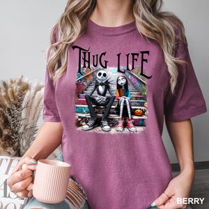 Puede incluir: Una camiseta morada con un gr&aacute;fico de Jack Skellington y Sally de Pesadilla Antes de Navidad sentados en un tramo de escaleras con grafitis. El texto "Thug Life" est&aacute; por encima de ellos.