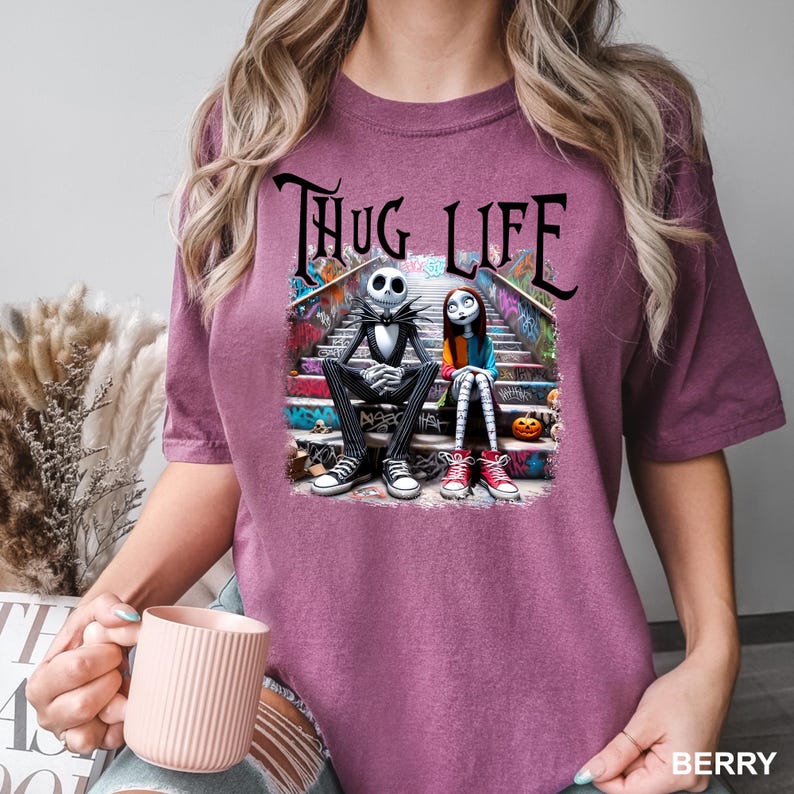 Puede incluir: Una camiseta morada con un gr&aacute;fico de Jack Skellington y Sally de Pesadilla Antes de Navidad sentados en un tramo de escaleras con grafitis. El texto "Thug Life" est&aacute; por encima de ellos.