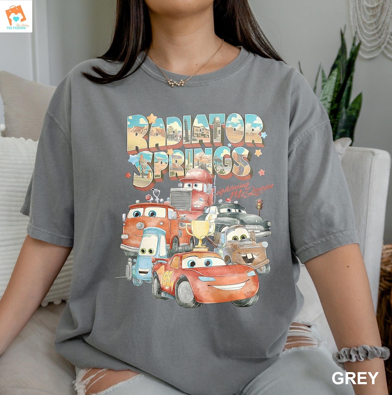 May include: A gray t-shirt with a graphic print of cartoon cars from the movie Cars. The text "Radiator Springs" is printed in a vintage style font.