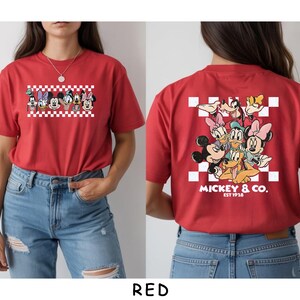 May include: A red t-shirt featuring a front graphic of Disney characters in a row over a white and red checkerboard pattern. The back displays a larger group of Disney characters over a checkerboard square with the text MICKEY & CO. EST 1928.