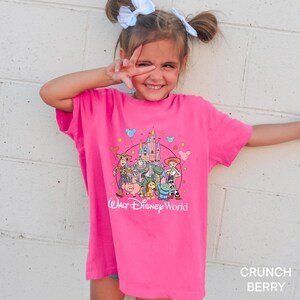 Puede incluir: Una camiseta rosa brillante con un gr&aacute;fico de los personajes de Toy Story de Disney y el castillo de Cenicienta, con el texto "Walt Disney World". La camiseta es de un tono rosa vibrante.