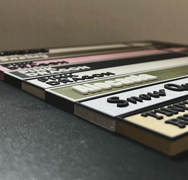 May include: A set of colorful, rectangular labels with different names printed on them, including "Pink Dragon", "Alcatraz", "Snow Queen", and "Timeless Beauty".