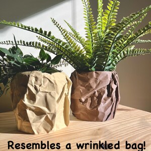May include: Two potted plants with green leaves in brown and beige crumpled paper pots that resemble wrinkled bags.
