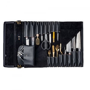May include: A black leather roll-up case with a variety of kitchen tools, including knives, scissors, and spatulas. The case has a flap that folds over the tools and secures with a strap.