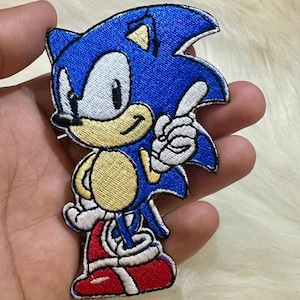 May include: An embroidered patch of Sonic the Hedgehog, a popular video game character. The patch features Sonic's signature blue fur, yellow gloves, and red shoes.