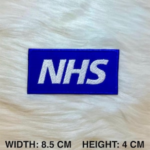 May include: Blue embroidered patch with white text that reads "NHS". The patch is 8.5 cm wide and 4 cm high.