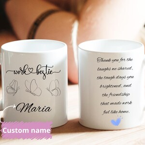 May include: White ceramic mug with the text "work bestie" and the name "Maria" in a script font, along with three butterfly illustrations. The mug also features the text "Thank you for the laughs we shared..." and a blue heart.