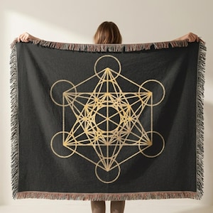 May include: A black throw blanket with a gold geometric design featuring circles and lines. The blanket has a fringed edge in shades of brown and red. The design is centered on the blanket.