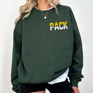 May include: A dark green sweatshirt with the word "PACK" printed in white letters with a yellow stripe across the middle of the word.