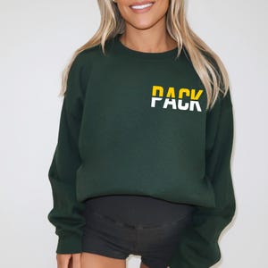 May include: A dark green sweatshirt with a white graphic that says "PACK" in yellow and white letters.