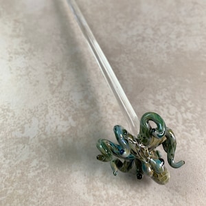 May include: A clear glass octopus-shaped drink stirrer with green and blue accents. The octopus has detailed tentacles and eyes. The stirrer has a long, clear stem, and is approximately 10 inches long.