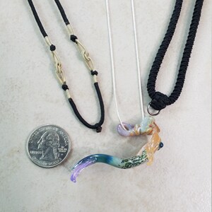 Pode incluir: Tr&ecirc;s colares com pingentes exclusivos. Um tem um cord&atilde;o preto com detalhes dourados, outro tem uma corrente prateada e o terceiro tem um cord&atilde;o preto. Os pingentes s&atilde;o coloridos, com um design abstrato curvo. Uma moeda est&aacute; inclu&iacute;da para refer&ecirc;ncia de tamanho.
