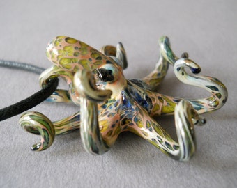 May include: A glass octopus pendant with a black cord. The octopus is multi-colored with shades of green, blue, pink, and white.
