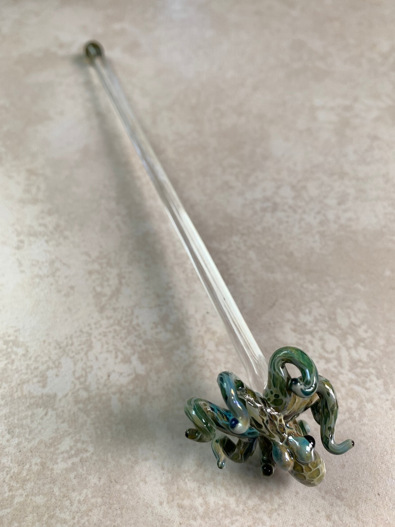 May include: A clear glass octopus-shaped drink stirrer with green and blue accents. The octopus has detailed tentacles and eyes. The stirrer has a long, clear stem, and is approximately 10 inches long.