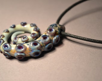 May include: A necklace with a ceramic octopus pendant. The octopus is curled up and has a blue, white, and purple color scheme.