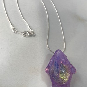 May include: A silver chain necklace with a purple glass pendant. The pendant is shaped like a blob with gold glitter inside.
