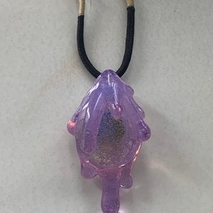 May include: A purple glass pendant necklace with a dripping design. The necklace is made with a black cord and a beige and brown cord.