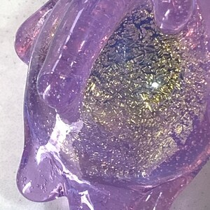 May include: A purple glass hand with a sparkly gold and purple interior. The hand is holding a small, round object.
