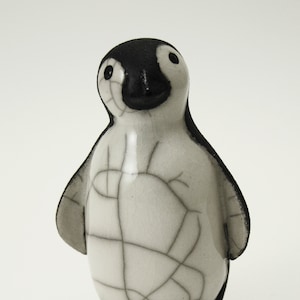 Può includere: Una piccola statuina di pinguino in ceramica con smalto bianco e nero. Il pinguino ha un corpo bianco con occhi, becco e piedi neri. Lo smalto ha un effetto craquelé, che conferisce al pinguino una texture unica.