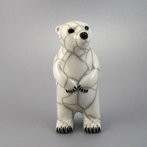 May include: A ceramic polar bear figurine with a distinctive cracked glaze pattern. The bear is white with black detailing on the eyes, nose, and paws. The figurine stands upright with its paws clasped, a charming decorative item.