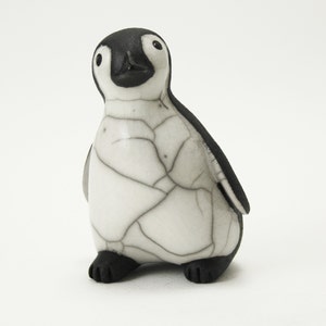 May include: A ceramic penguin ornament. It has a black head, wings, and feet, and a white body with a cracked pattern. The penguin has a small beak and is standing upright.