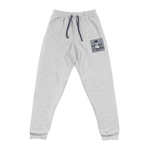 May include: Light gray sweatpants with an elastic waistband and dark gray drawstring. A square patch on the right leg features a graphic of a seagull wearing a hat and the text "Gabbiani si diventa" printed in black lettering on a gray background.