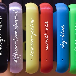 Op de afbeelding: Zeven verschillende gekleurde plastic buizen met witte tekst op elke buis. De tekst luidt: midnight-black, diffuse-transparent, lemon-yellow, sunset-red, sky-blue, lime-green.