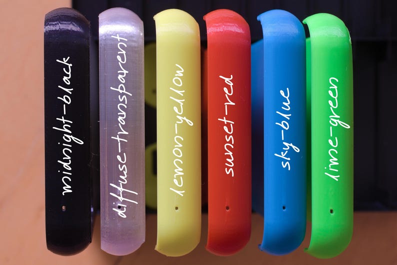 Op de afbeelding: Zeven verschillende gekleurde plastic buizen met witte tekst op elke buis. De tekst luidt: midnight-black, diffuse-transparent, lemon-yellow, sunset-red, sky-blue, lime-green.