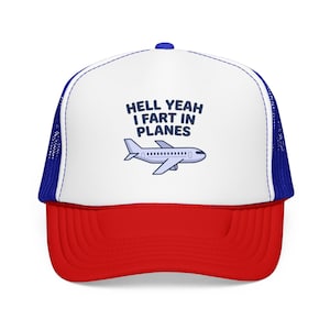 Pode incluir: Um boné trucker com painel frontal branco, aba vermelha e painéis traseiros de rede azul. A frente apresenta um gráfico de um avião azul claro e o texto HELL YEAH I FART IN PLANES impresso em letras azul-escuras no painel branco.