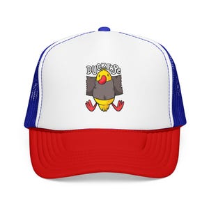 Può includere: Un cappellino trucker con pannello frontale bianco, retro in rete blu e visiera rossa. La parte anteriore presenta la grafica di un'anatra gialla con becco rosso avvolta in nastro grigio, con la scritta DUCKTAPE stampata in nero.