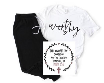May include: A white t-shirt with the word "worthy" written in black cursive with a small heart above it. A black and white graphic with a wreath of leaves and hearts around the text "The Overflow Boutique by The Scotts Tomball, TX Psalms 23:5" with a cross at the bottom.