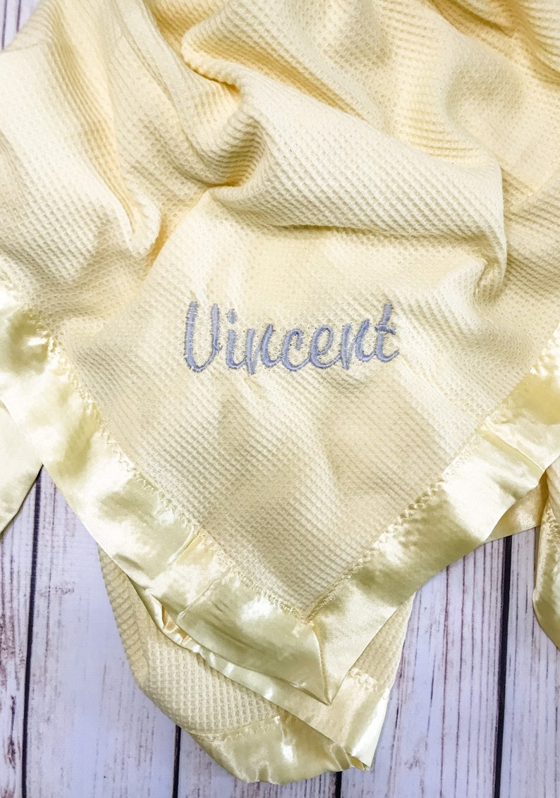 May include: A yellow waffle weave baby blanket with a satin trim and the name "Vincent" embroidered in gray.