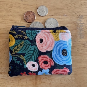 May include: A small zippered pouch with a floral print. The pouch is made of fabric and has a dark blue background with pink, blue, yellow, and green flowers.
