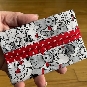 Puede incluir: Un porta pañuelos blanco con una cinta roja con lunares blancos. La tela tiene un patrón de perros en blanco y negro.