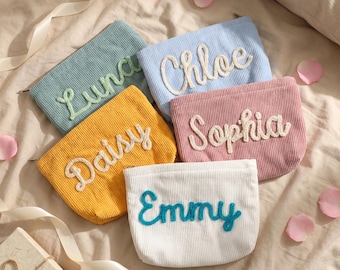 May include: Five corduroy pouches in pastel colors: light blue, pink, yellow, white, and teal. Each pouch has a name embroidered in a contrasting color: Luna, Chloe, Sophia, Daisy, and Emmy. The pouches are arranged on a bed with rose petals.