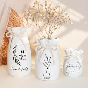 May include: Three white ceramic vases of varying sizes, each adorned with a cream-colored rope bow. The largest vase has the text "9 years of us" and the names "Jason & Emily". The middle vase has the initials "j + h" and the date "03.20.25". The smallest vase has two elephants.