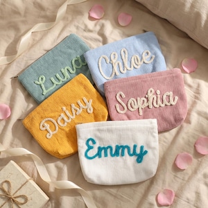 May include: Five corduroy pouches in pastel colors: light blue, pink, yellow, white, and teal. Each pouch has a name embroidered in a contrasting color: Luna, Chloe, Sophia, Daisy, and Emmy. The pouches are arranged on a bed with rose petals.