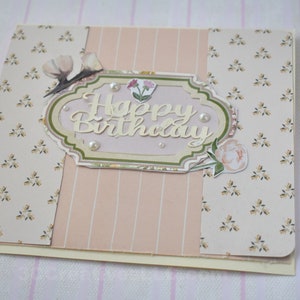 4 x 5.5 inch card in Peach floral and striped printed paper. Happy Birthday cutout in center  decorated with fussy cut flowers and white pearls .