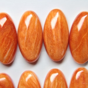 Peut inclure: Huit cabochons ovales de couleur orange et blanche avec un motif marbré. Les cabochons sont lisses et polis.