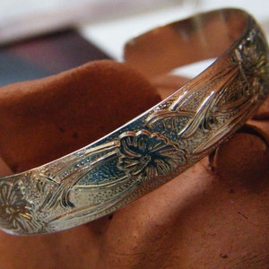 May include: A silver bangle bracelet with an intricate floral design. The bracelet is smooth and shiny, with a delicate floral pattern etched into the metal.