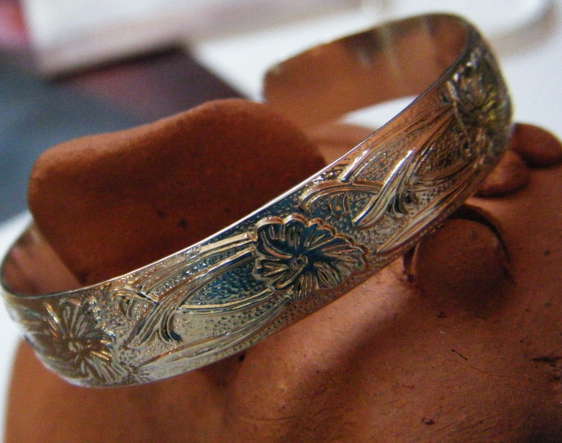 May include: A silver bangle bracelet with an intricate floral design. The bracelet is smooth and shiny, with a delicate floral pattern etched into the metal.