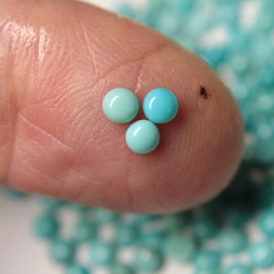 Puede incluir: Tres piedras redondas de cabujón azul turquesa en la yema de un dedo. Las piedras tienen un diámetro aproximado de 5 mm.