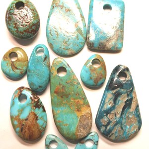 May include: A collection of eleven polished turquoise pendants in various shapes and sizes, each featuring a drilled hole at the top. The stones display natural variations in blue, green, and brown matrix patterns with a smooth, glossy finish.
