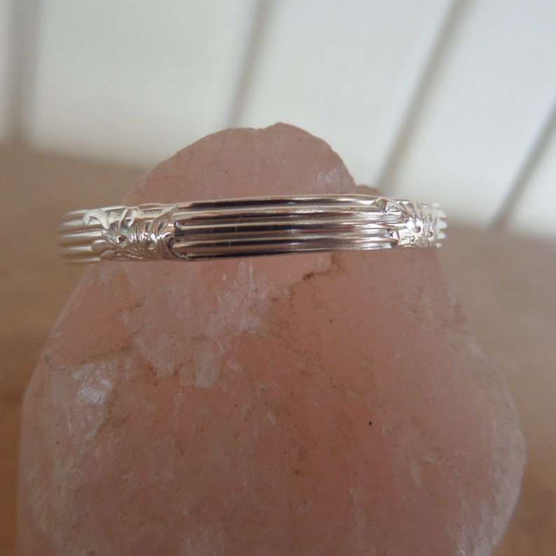 Pode incluir: Um anel de prata com um design texturizado. O anel est&aacute; sobre uma superf&iacute;cie rosa.
