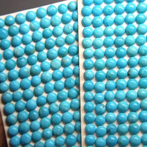 May include: Two rectangular sheets filled with numerous small, round, light blue turquoise gemstones. The gemstones are evenly spaced and set on a white backing, creating a pattern. The image is a close-up.