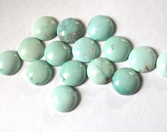 May include: A collection of round, polished turquoise gemstones. The stones vary in shades of blue-green, with some showing natural veining and markings. They are arranged on a white surface, showcasing their smooth, domed surfaces.