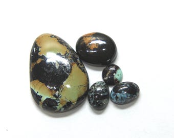 May include: A collection of five polished, oval-shaped cabochon gemstones featuring a mix of deep black, tan, and turquoise blue matrix patterns. The stones vary in size, with one large prominent piece and four smaller stones arranged nearby.