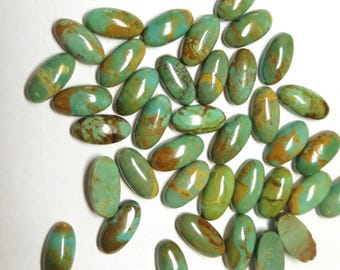 May include: A collection of numerous oval-shaped turquoise gemstones scattered across the frame. Each stone features a polished, smooth surface with a distinct blend of vibrant teal, light green, and earthy brown matrix veining throughout.