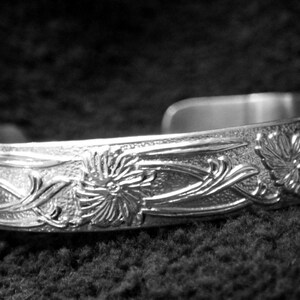 May include: A silver bracelet with an intricate floral design. The bracelet is made of metal and has a polished finish.