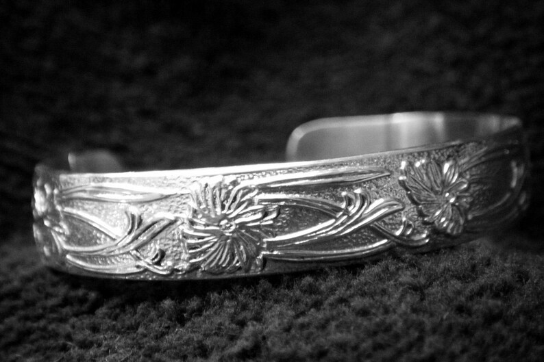 May include: A silver bracelet with an intricate floral design. The bracelet is made of metal and has a polished finish.